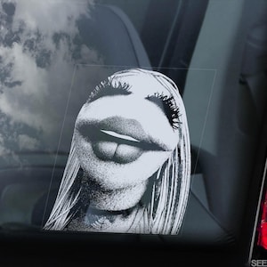 May include: A black and white vinyl decal featuring a stylised, high-contrast portrait of a character with long hair, prominent eyelashes, and full lips, applied to a smooth, transparent surface, showing a detailed, stippled graphic design.