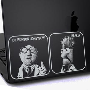 May include: A black sticker featuring Dr. Bunsen Honeydew and Beaker from The Muppets. The sticker is applied to a black laptop. The text "Dr. Bunson Honeydew" and "Beaker" are visible.