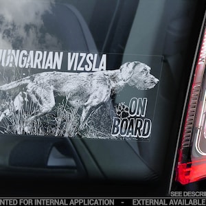 Könnte beinhalten: Ein weißer Autofenstersticker mit einer Schwarzweißillustration eines Ungarischen Vizsla-Hundes, der durch hohes Gras rennt. Der Text "HUNGARIAN VIZSLA ON BOARD" ist in schwarzen Buchstaben gedruckt.
