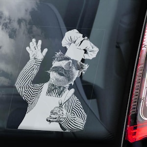 Puede incluir: Gráfico en blanco y negro del Chef sueco de los Muppets, saludando y sosteniendo un cuchillo. El chef lleva una camisa a rayas, un delantal y un gorro de chef. La imagen está en la ventana de un coche con un cielo nublado de fondo.