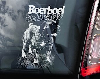 Peut inclure: Un autocollant transparent avec le texte "Boerboel On Board" et une illustration détaillée d'un chien Boerboel. L'autocollant est placé sur une vitre de voiture, avec le ciel et un feu arrière en arrière-plan.