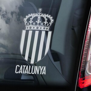 Puede incluir: Una pegatina blanca y negra con un diseño de corona y escudo. El escudo tiene rayas verticales y el texto "CATALUNYA" está debajo del escudo.