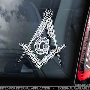 May include: A white vinyl sticker of a Masonic compass and square with a 'G' in the centre. The sticker is on a car window.
