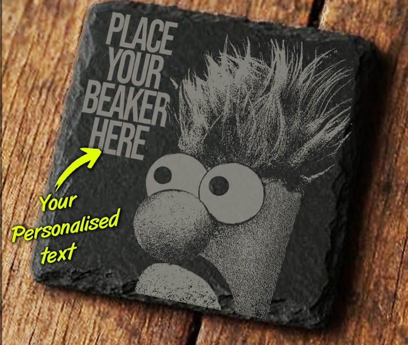 May include: A square, black slate coaster with a cartoon character design. The design features a character with large eyes and a prominent nose, with the text "PLACE YOUR BEAKER HERE". A yellow arrow points to the text, with the words "Your Personalised text".