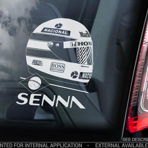 Puede incluir: Una pegatina blanca y negra con un casco de carreras con el texto "NACIONAL", "Mar", "HON", "GHEDS", "BOSS HENG FASHION" y "NACIO". La pegatina también incluye el texto "SENNA" en una fuente grande.