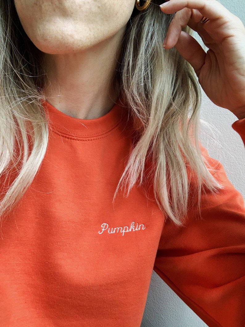 May include: A bright orange sweatshirt with the word "Pumpkin" embroidered in white on the front.