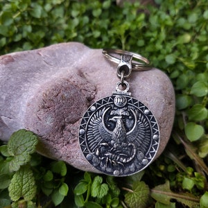 May include: Silver keyring with a round pendant depicting a phoenix rising from a scorpion. The pendant is encircled by a ring of small dots and the Roman numeral III is visible at the top.
