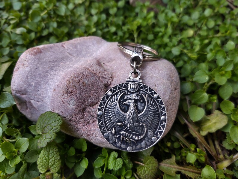 May include: Silver keyring with a round pendant depicting a phoenix rising from a scorpion. The pendant is encircled by a ring of small dots and the Roman numeral III is visible at the top.