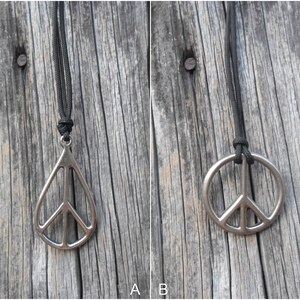 May include: Two silver peace sign pendants on black cords. The pendant on the left is a teardrop shape, while the pendant on the right is a circle.