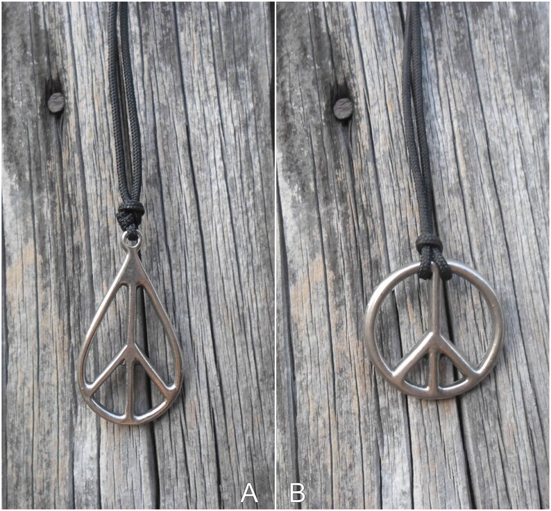 May include: Two silver peace sign pendants on black cords. The pendant on the left is a teardrop shape, while the pendant on the right is a circle.