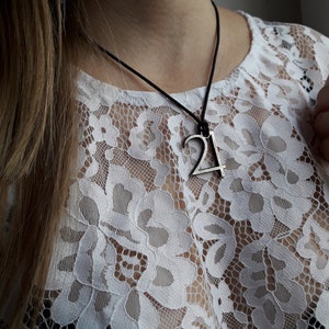 Puede incluir: Primer plano de un collar de plata con un colgante en forma del número 21. El collar lo lleva una persona con el pelo largo y castaño y una blusa de encaje blanca.