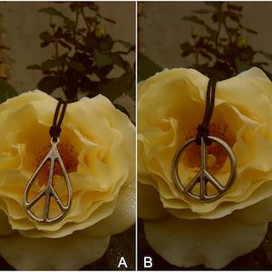 May include: A silver peace sign pendant necklace on a black cord, resting on a yellow rose.
