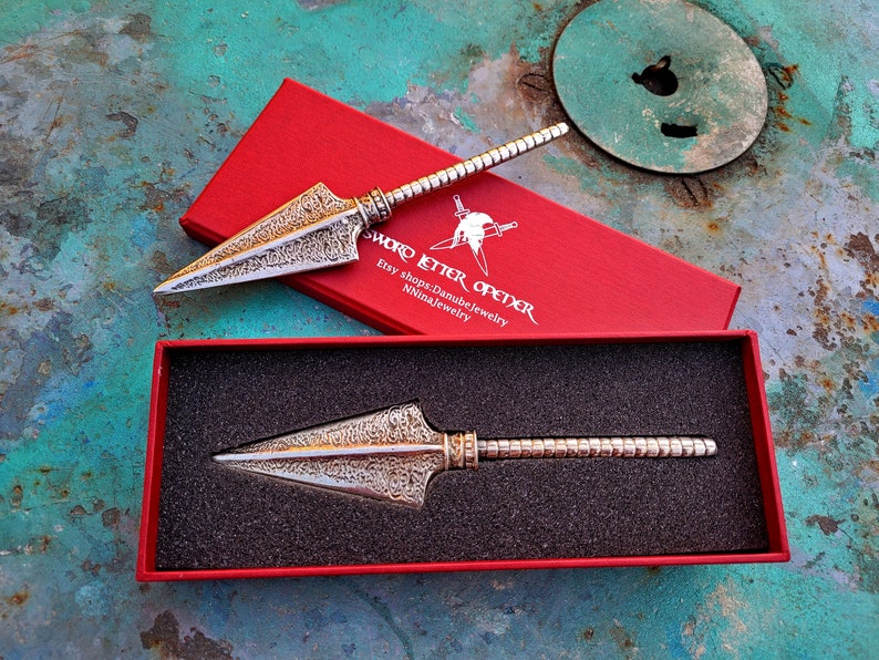 May include: Two silver sword letter openers in red boxes. The boxes have the text "Sword Letter Opener" and "Etsy shops: Danubejewelry Ninajewelry".