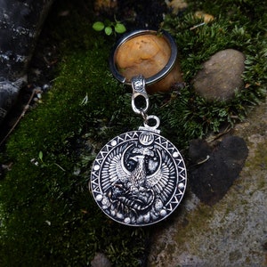 May include: Silver key chain with a round metal charm featuring a detailed design of a phoenix with its wings spread. The charm is surrounded by a decorative border.