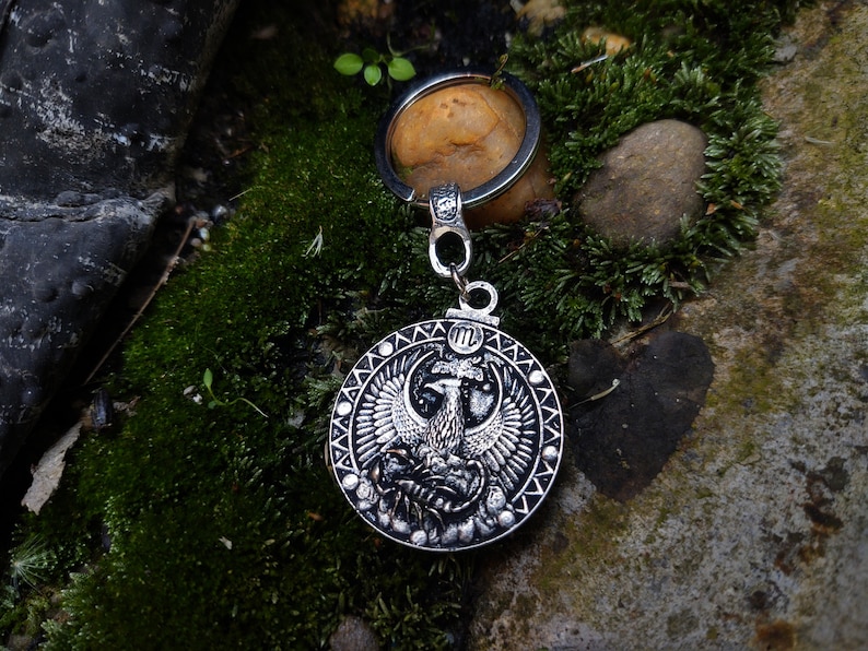 May include: Silver key chain with a round metal charm featuring a detailed design of a phoenix with its wings spread. The charm is surrounded by a decorative border.