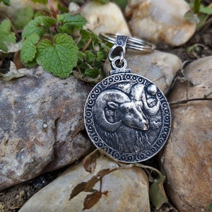 May include: Silver key chain with a round charm featuring a detailed ram head design. The charm is surrounded by a decorative border.