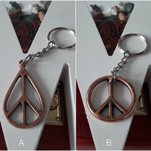 May include: Two peace sign keychains, one with a teardrop shape and the other a circle, both made of copper-toned metal. The keychains are attached to silver key rings.