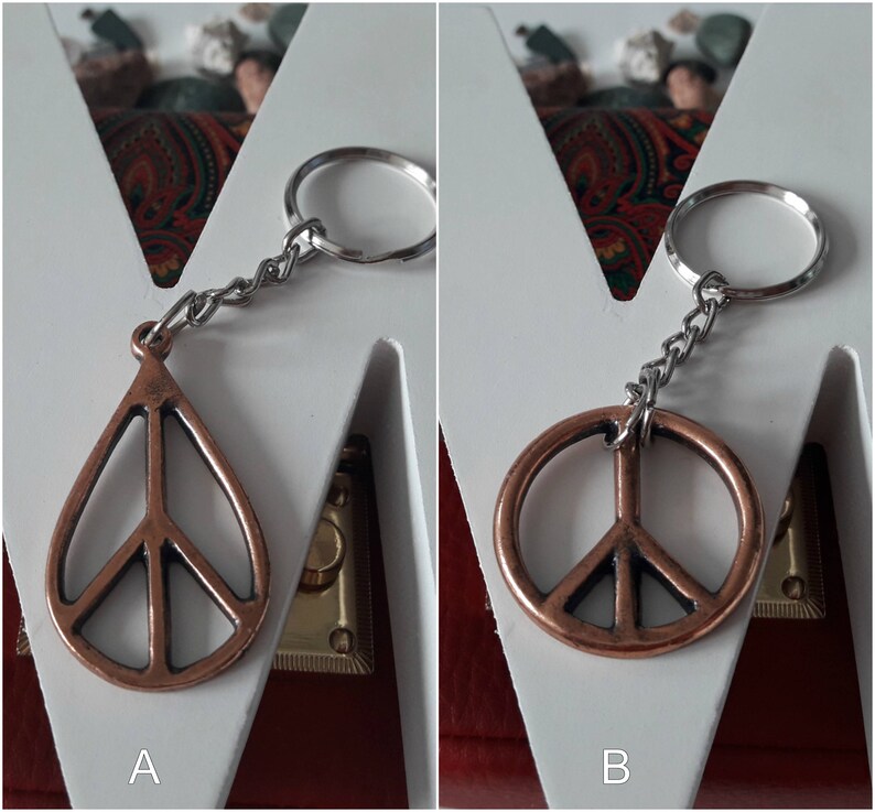 May include: Two peace sign keychains, one with a teardrop shape and the other a circle, both made of copper-toned metal. The keychains are attached to silver key rings.