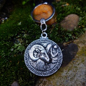 May include: Silver-toned keychain featuring a detailed ram's head design. The ram's head is surrounded by a circular border with a repeating pattern of small circles.