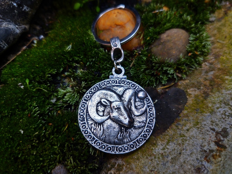 May include: Silver-toned keychain featuring a detailed ram's head design. The ram's head is surrounded by a circular border with a repeating pattern of small circles.