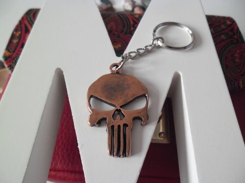 Pode incluir: Um chaveiro de caveira de cor cobre com uma corrente e um anel prateados. A caveira tem um design detalhado com uma superf&iacute;cie texturizada em relevo.