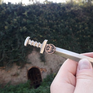 May include: A silver-colored miniature sword with a copper-colored eagle emblem on the pommel.