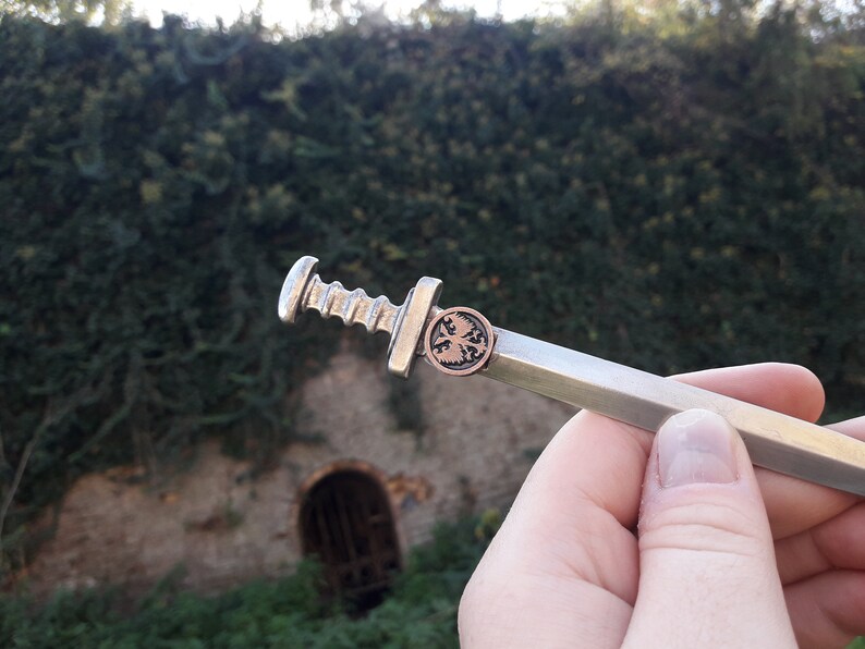 May include: A silver-colored miniature sword with a copper-colored eagle emblem on the pommel.