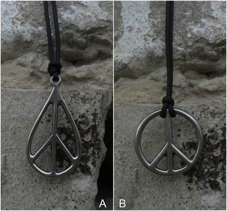 May include: Two silver peace sign pendants on black cords. The pendant on the left is a teardrop shape, while the pendant on the right is a circle.