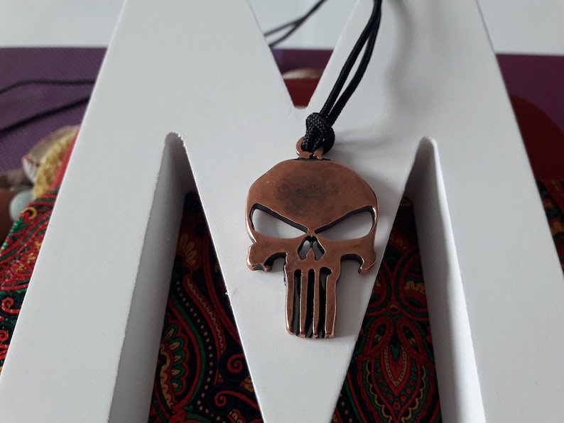 Pode incluir: Um pingente de caveira de cor cobre com um cord&atilde;o preto. A caveira tem um design detalhado com uma mand&iacute;bula proeminente e uma superf&iacute;cie texturizada.