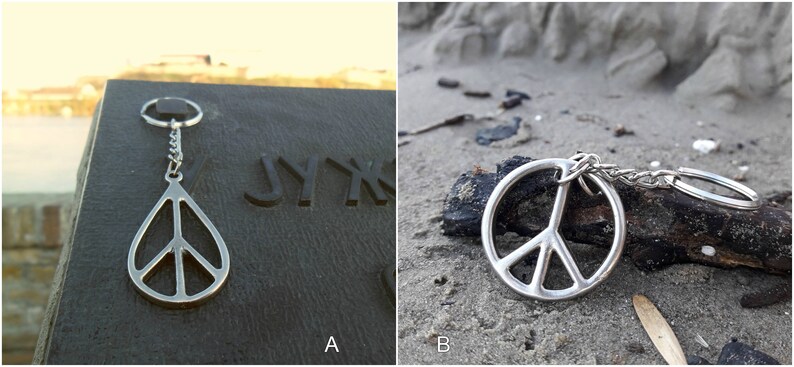 May include: Two images of a silver peace sign keychain. The first image shows the keychain on a dark surface with the word "JYKK" engraved on the surface. The second image shows the keychain on a sandy surface with a piece of driftwood.