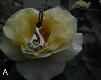 May include: A silver pendant in the shape of a hook hangs from a black cord. The pendant is resting on a white rose with water droplets.