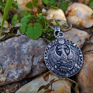 May include: Silver key chain with a round charm featuring a detailed image of a phoenix rising from a scorpion. The charm has a black and white design and the zodiac symbol for Scorpio, "♏", is engraved on the top.