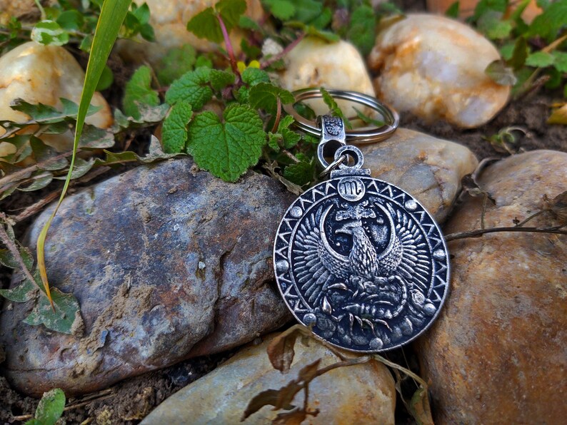May include: Silver key chain with a round charm featuring a detailed image of a phoenix rising from a scorpion. The charm has a black and white design and the zodiac symbol for Scorpio, "♏", is engraved on the top.