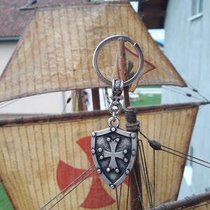 May include: Silver keychain with a shield-shaped charm featuring a cross and a red cross on a model ship.
