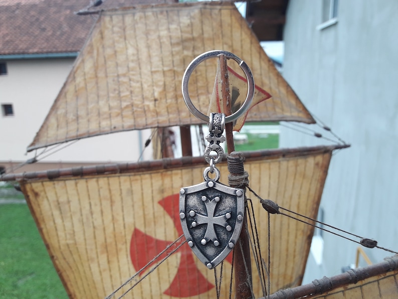 May include: Silver keychain with a shield-shaped charm featuring a cross and a red cross on a model ship.