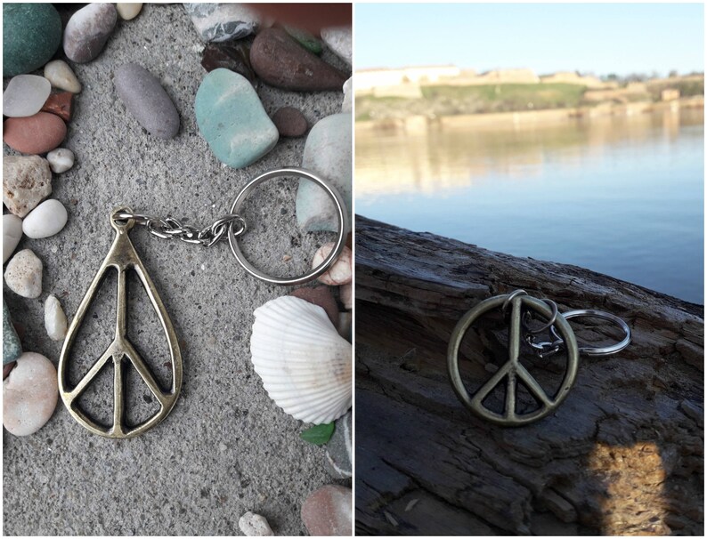 May include: A silver peace sign keychain with a silver ring and a gold peace sign charm. The keychain is on a gray background with small stones and a white seashell.
