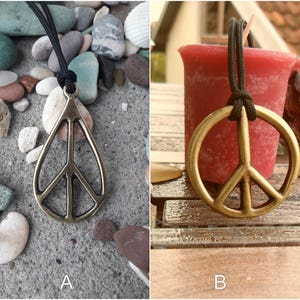 May include: Two images of a gold peace sign pendant necklace. The first image shows the necklace on a gray background with small stones. The second image shows the necklace on a wooden surface with a red candle.