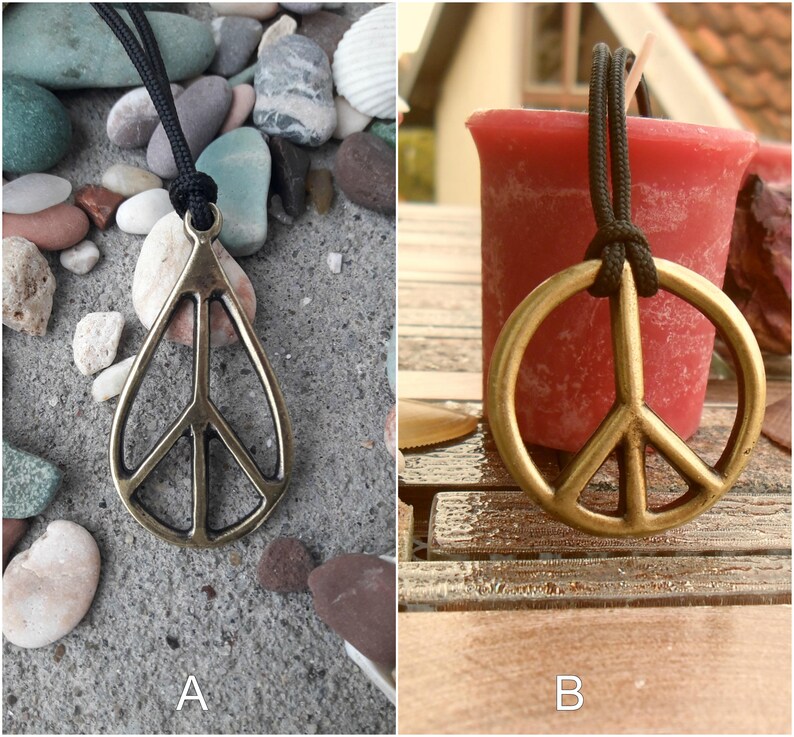 May include: Two images of a gold peace sign pendant necklace. The first image shows the necklace on a gray background with small stones. The second image shows the necklace on a wooden surface with a red candle.