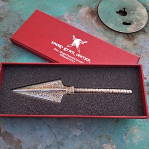 May include: A silver bottle opener in the shape of a spearhead, with a textured surface, in a red velvet box. The box has the text "SWORD LETTER OPENER" and "Etsy shop: DanubeJewelry" printed on the lid.