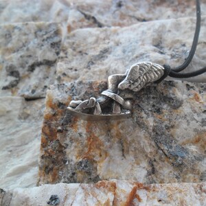 May include: A silver pendant necklace featuring a winged sandal, a symbol of the Greek god Hermes. The pendant is attached to a black cord.