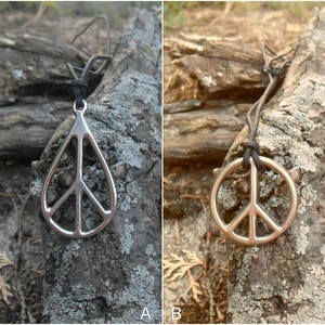 May include: A silver peace sign pendant necklace on a black cord, hanging from a tree branch. The pendant is shaped like a teardrop with a peace sign inside.