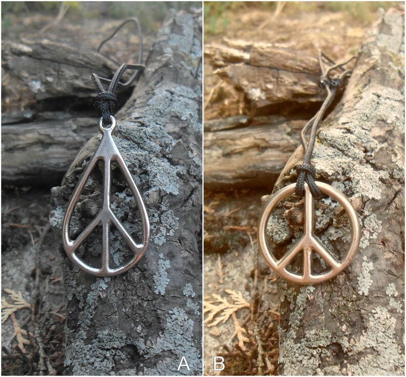 May include: A silver peace sign pendant necklace on a black cord, hanging from a tree branch. The pendant is shaped like a teardrop with a peace sign inside.