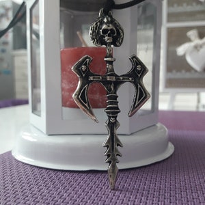 Può includere: Una collana con un ciondolo in argento che presenta un teschio con una corona e una spada con due lame di ascia.