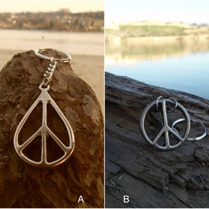 May include: Two silver peace sign keychains. The keychain on the left is a peace sign pendant on a silver chain. The keychain on the right is a peace sign charm on a silver ring.