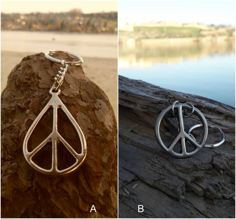 May include: Two silver peace sign keychains. The keychain on the left is a peace sign pendant on a silver chain. The keychain on the right is a peace sign charm on a silver ring.