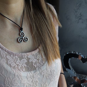 May include: A silver Celtic knot pendant necklace on a black cord. The pendant is a triple spiral design.