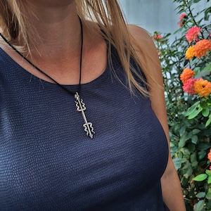 Puede incluir: Una mujer lleva un top sin mangas azul oscuro con un collar de plata con un colgante en forma de flecha de doble punta.