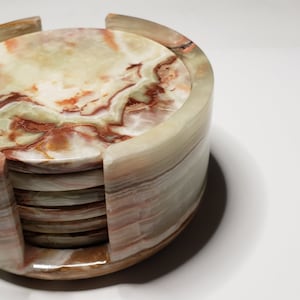 May include: Set of six round green and brown marble coasters in a matching holder. The coasters are stacked and the holder is made of the same material.