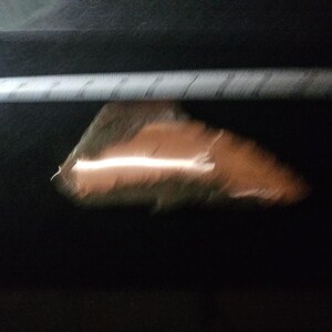 May include: A blurry image of a light-colored ruler and a brown object with a white streak. The background is dark.