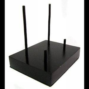 May include: Black wooden display stand with four vertical rods for displaying items. The stand has a square base and is made of wood.